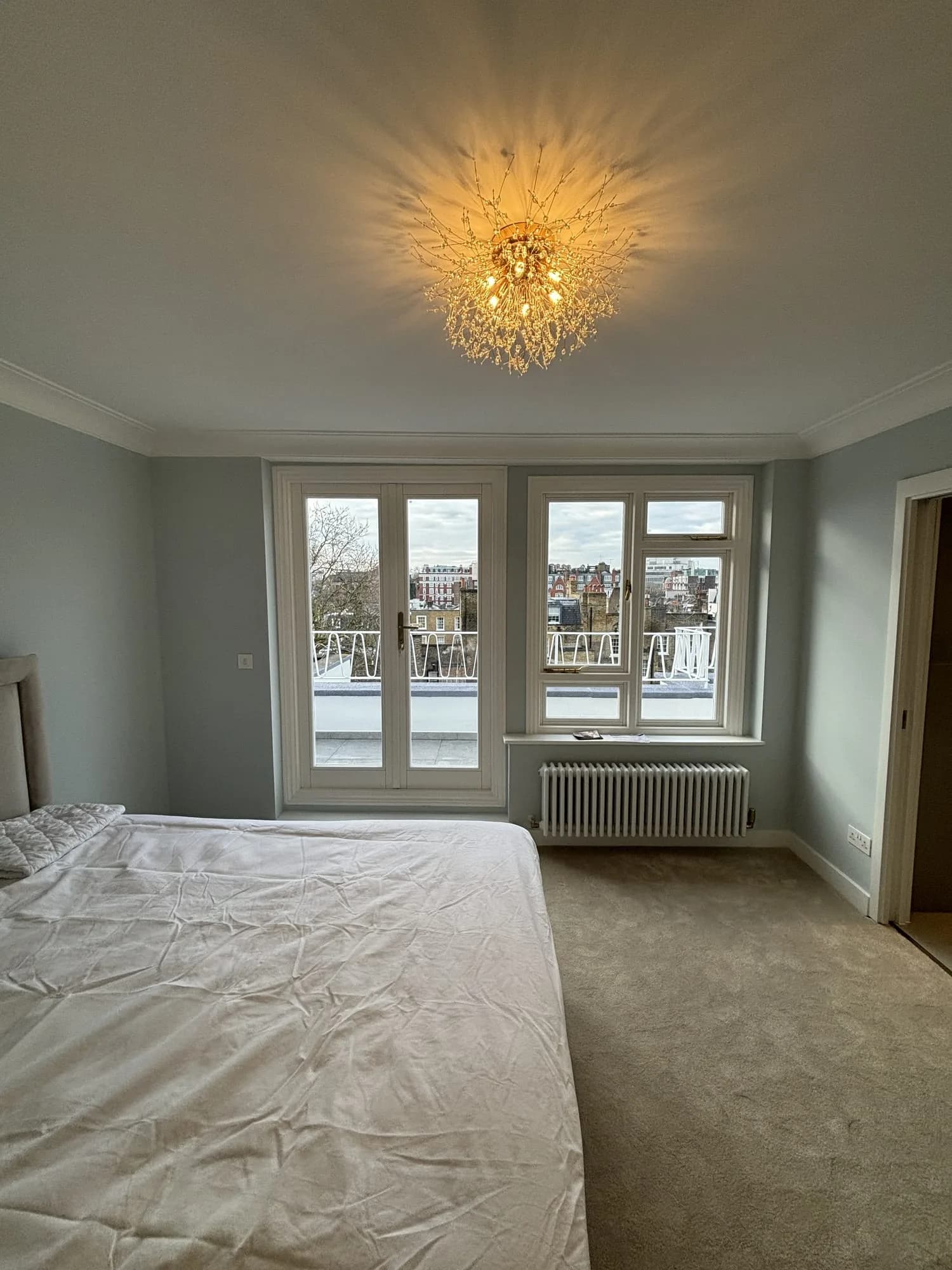 Belgravia: bedroom with a crystal chandelier and French doors onto a balcony