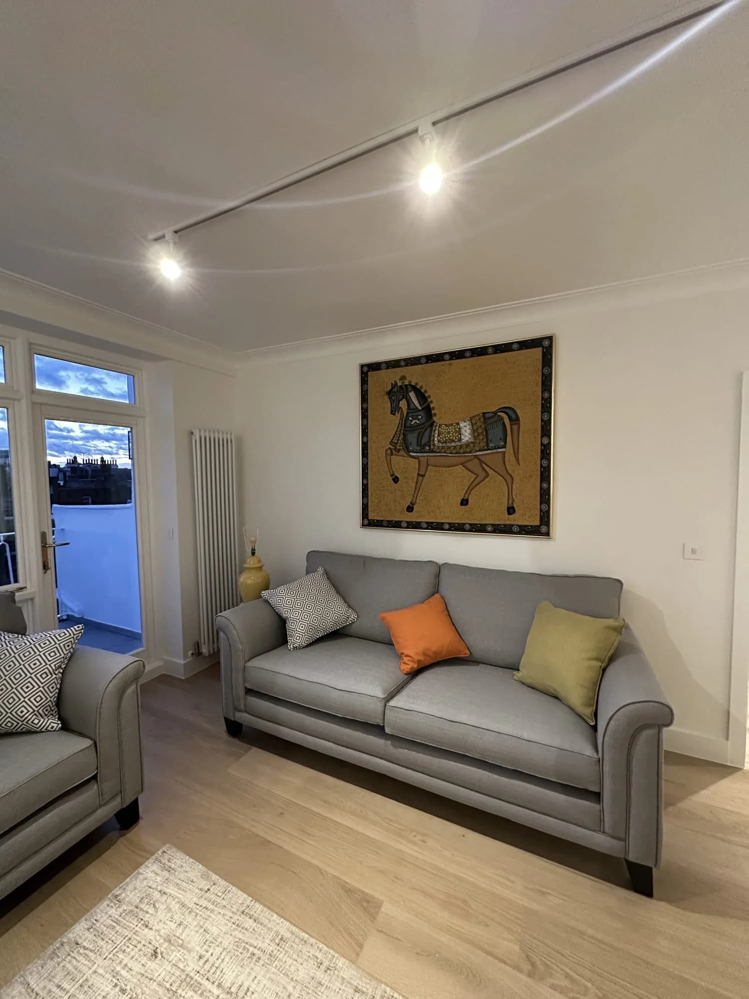 Belgravia: sitting room with a grey sofa, a framed tapestry and a door to the balcony