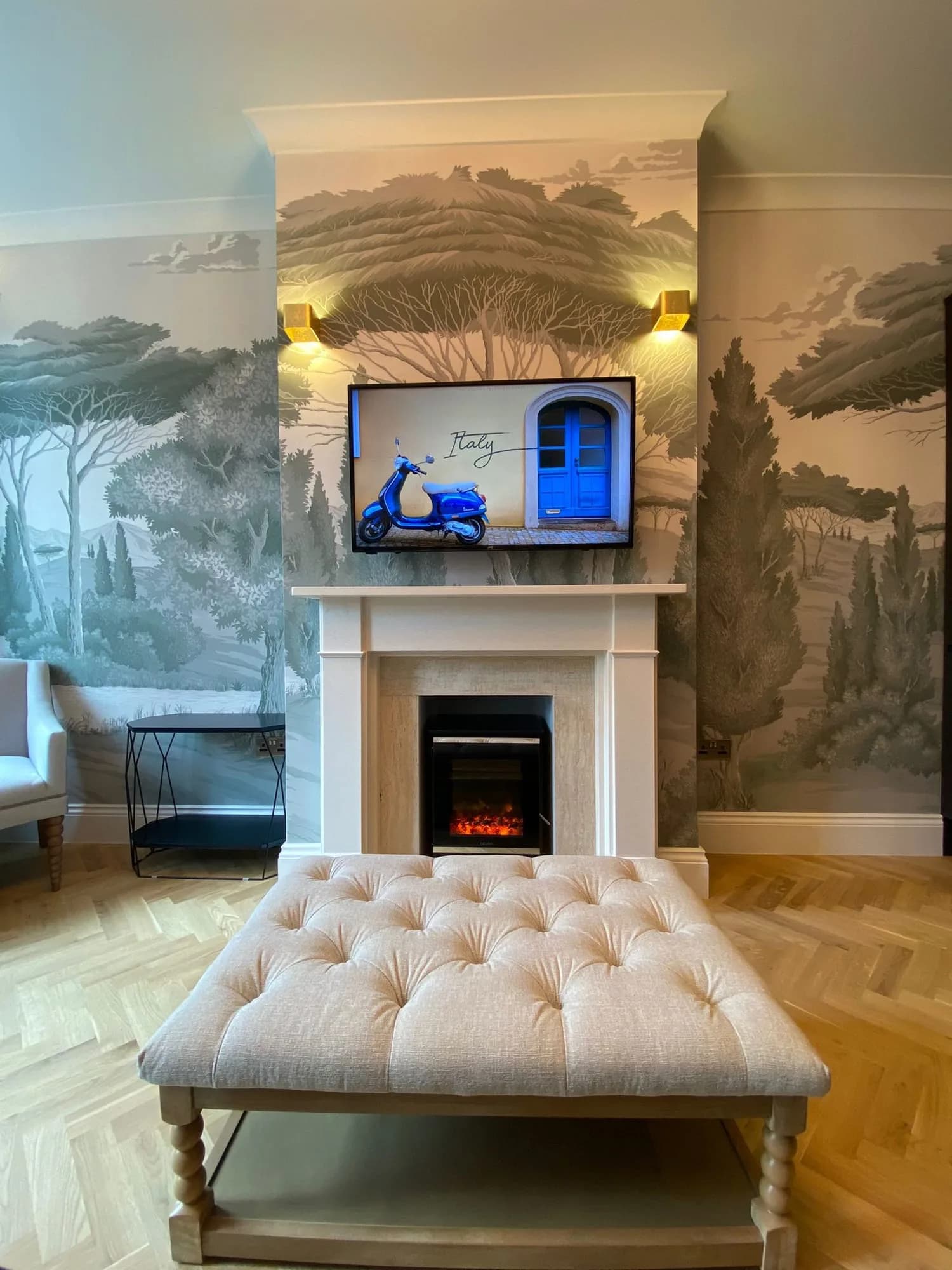Chelsea I: fireplace and buttoned ottoman on herringbone parquet, framed by mural walls