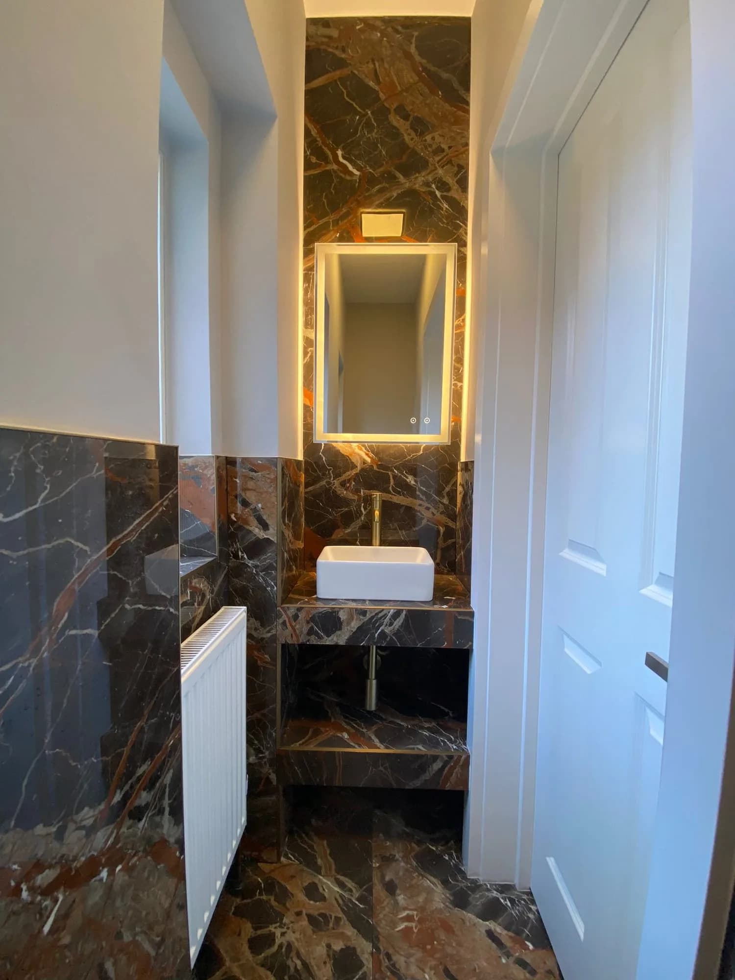 Chelsea I: cloakroom clad in figured brown marble with a backlit mirror and stone basin