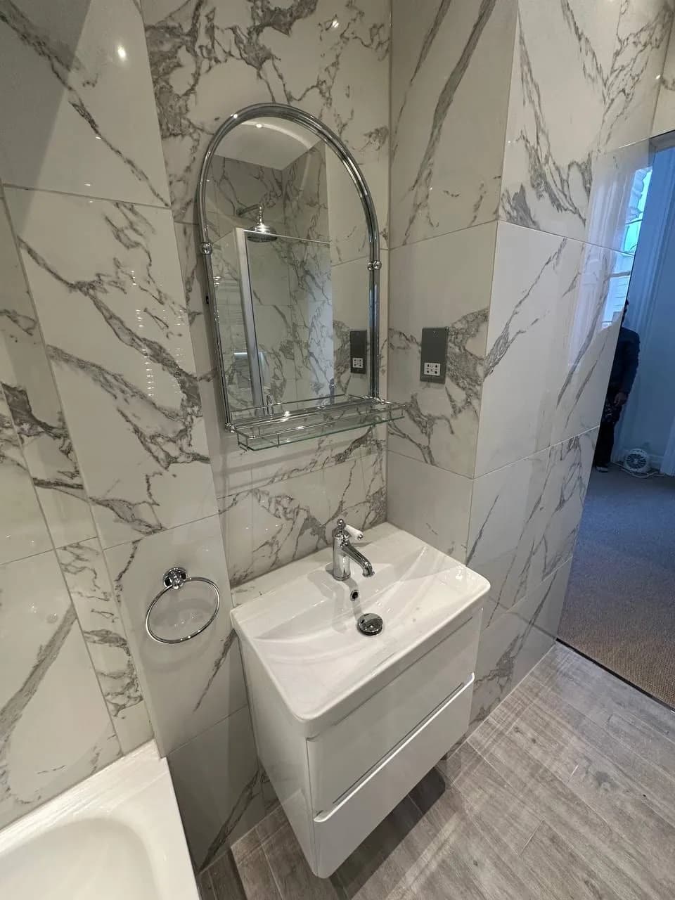Chelsea II: bathroom lined in veined marble-effect porcelain with an arched mirror