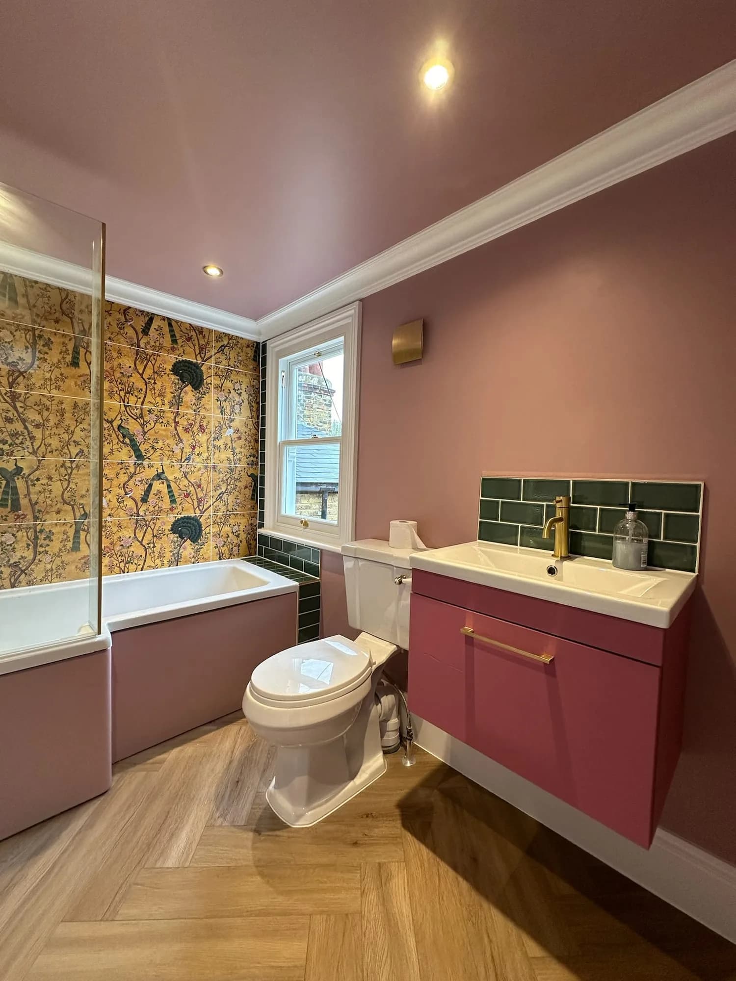 Earls Court II: pink bathroom with a green tiled splashback and patterned wallpaper