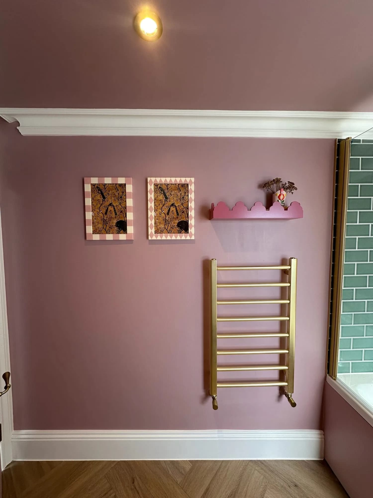 Earls Court II: pink bathroom wall with a brass towel radiator and framed prints