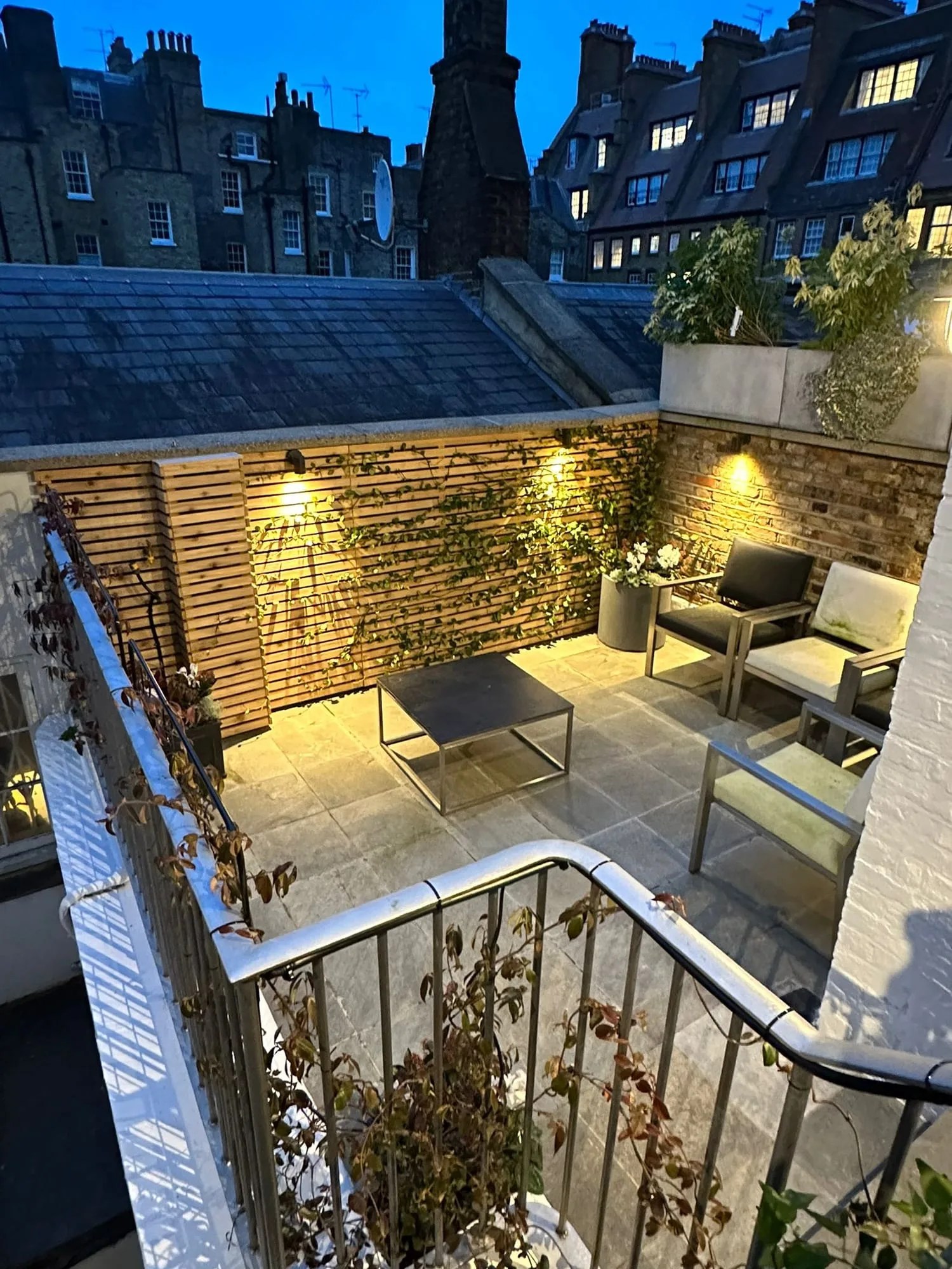 Chelsea II: roof terrace at dusk with lit brick walls, planting and seating