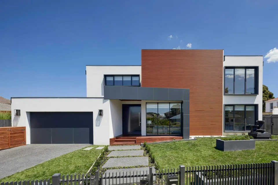 Front elevation of a rendered and timber-clad house behind a low railing and lawn