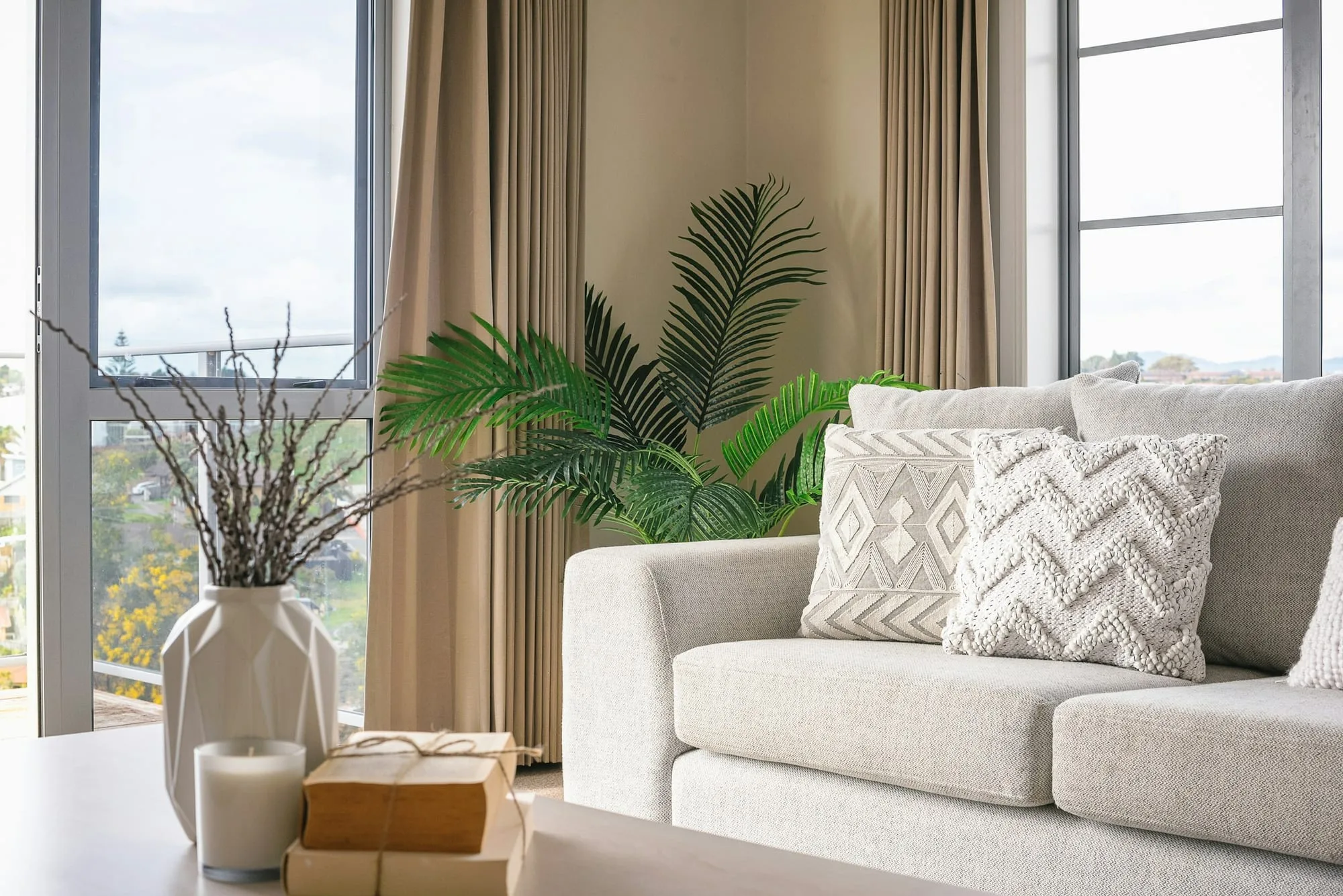 Neutral sofa with textured cushions beside a tall curtained window