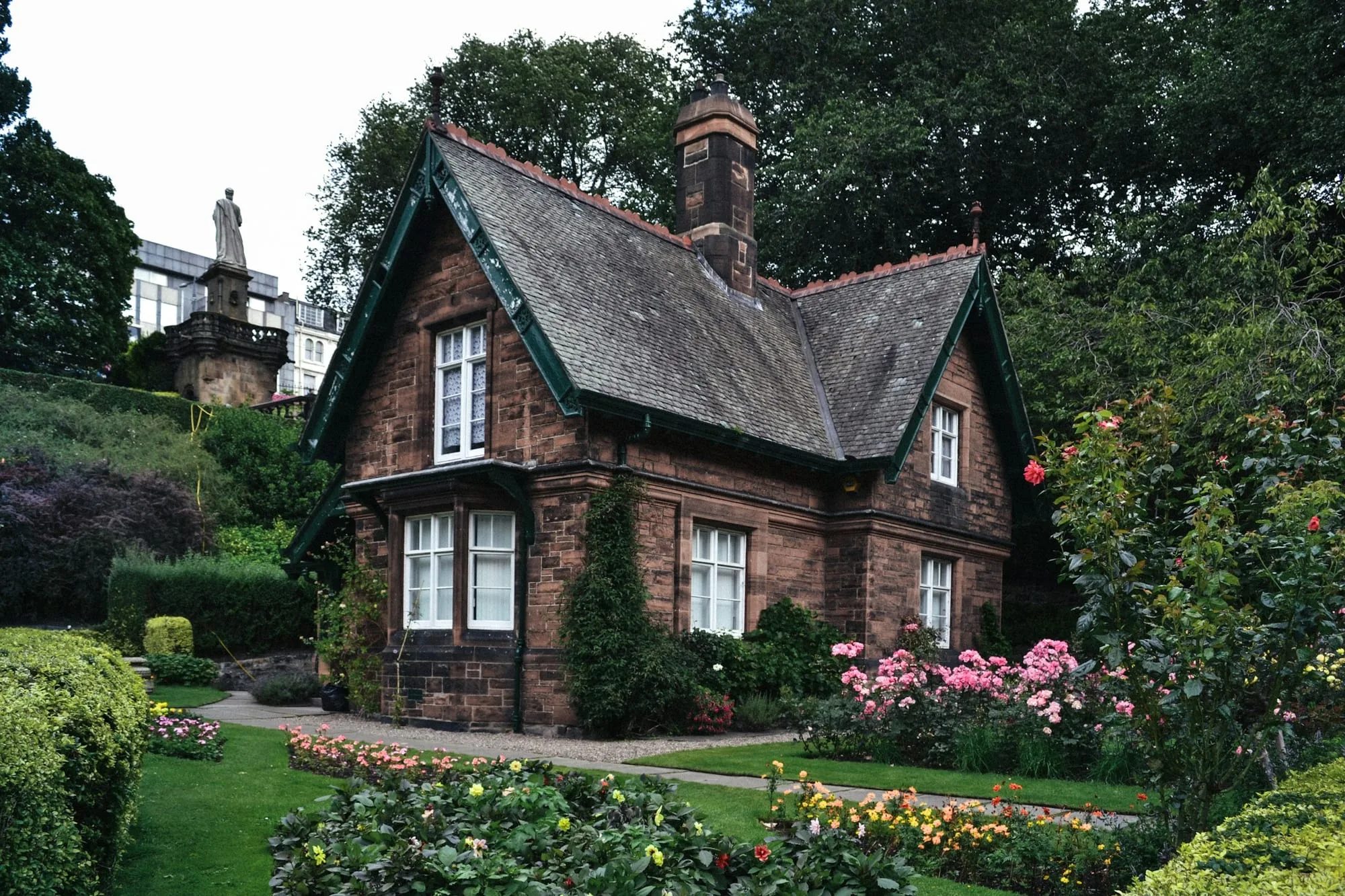 Victorian stone house with a steep tiled roof behind a planted garden