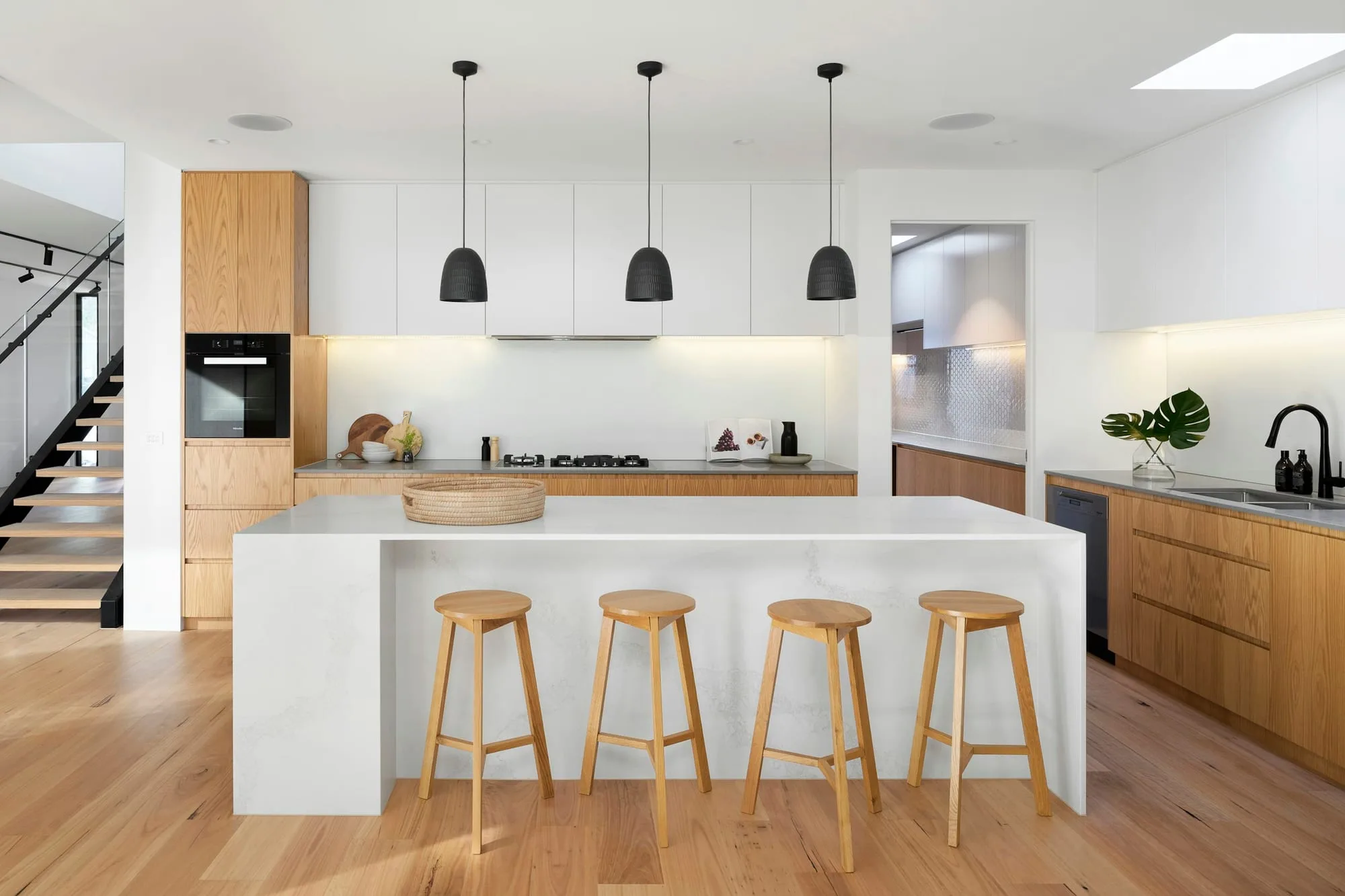 Modern kitchen with under-cabinet lighting, black pendants and a stone island with oak stools