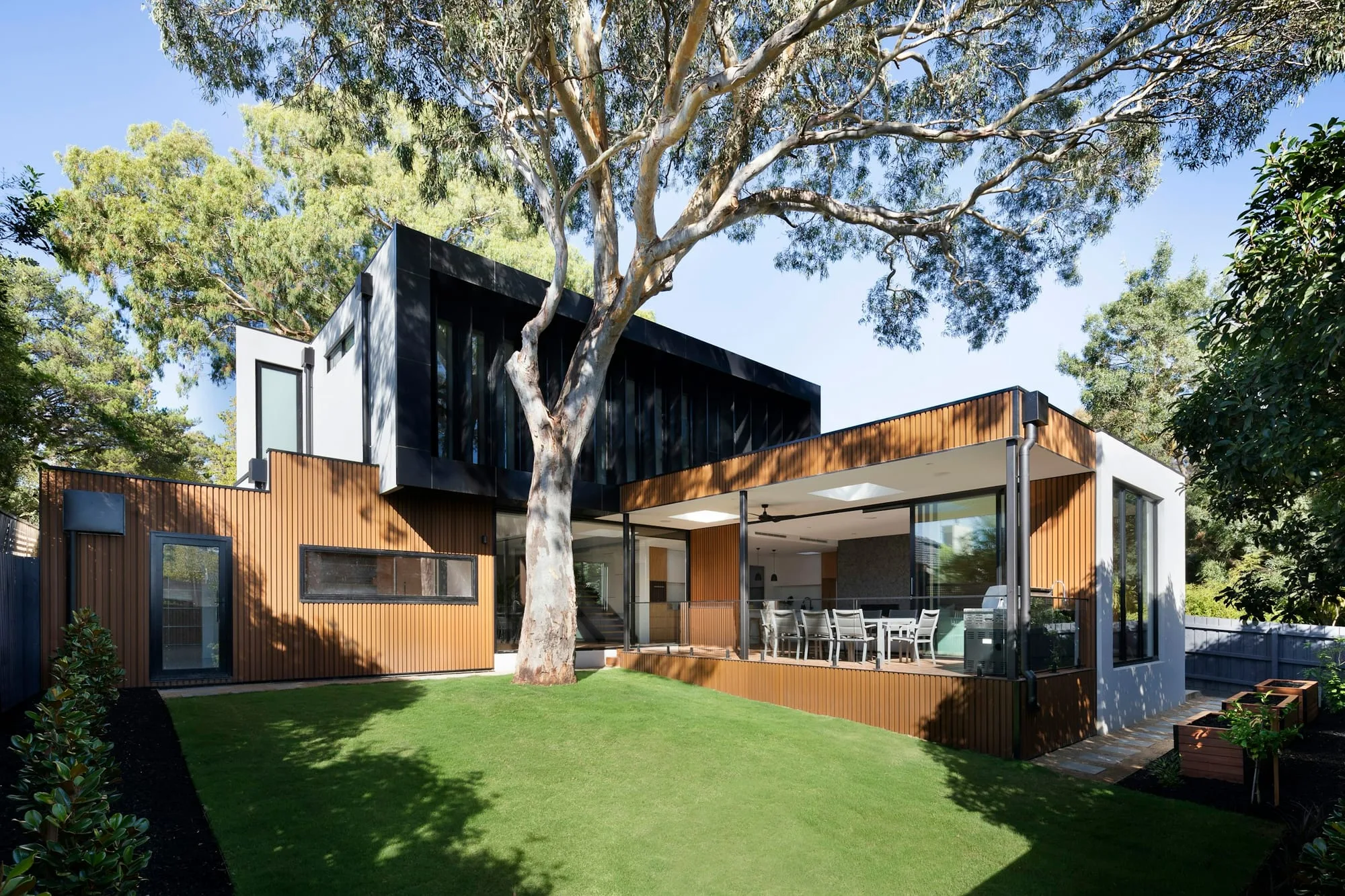 Rear extension in dark timber cladding with full-height glazing onto a lawn
